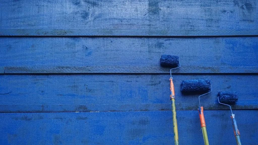 Three paint rollers leaning against a wall freshly painted blue
